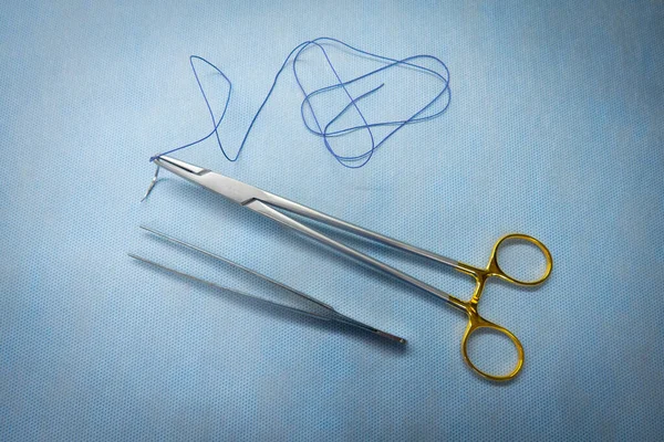 針ホルダーの中に外科的縫合糸がクランプされピンセットのペアが横に横たわっています — ストック写真