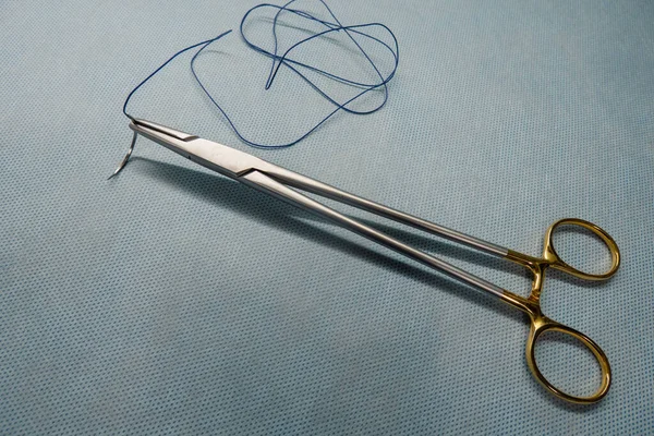 Cerrahi dikiş iğnenin sapına tutturulur ve yanında da bir çift cımbız bulunur.