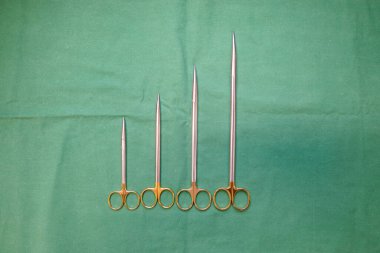 Farklı boyutlarda cerrahi makas yeşil bir zeminde yan yana yatar.