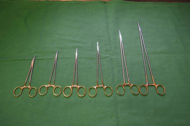 Farklı boyutlarda cerrahi iğne tutucuları yeşil bir zeminde yan yana yatar.