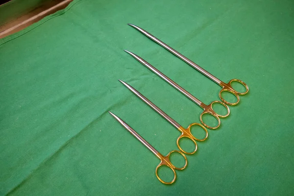 Farklı boyutlarda cerrahi makas yeşil bir zeminde yan yana yatar.