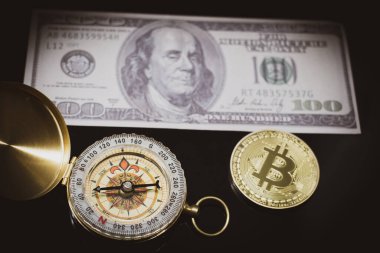 1 bitcoin pusula ve 100 dolarlık banknotun yanında duruyor.