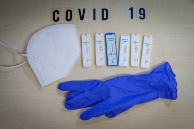 6 positive corona rapid tests lie next to a medical face mask and a blue medical glove