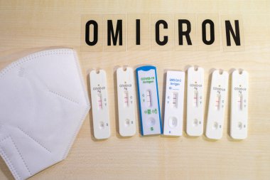 six positive corona rapid tests lie next to a medical face mask and above them is the word Omicron