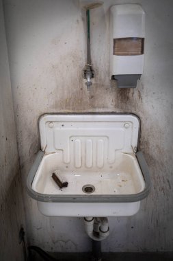 Bir atölyenin duvarında eski bir lavabo ve sabun makinesi asılı.