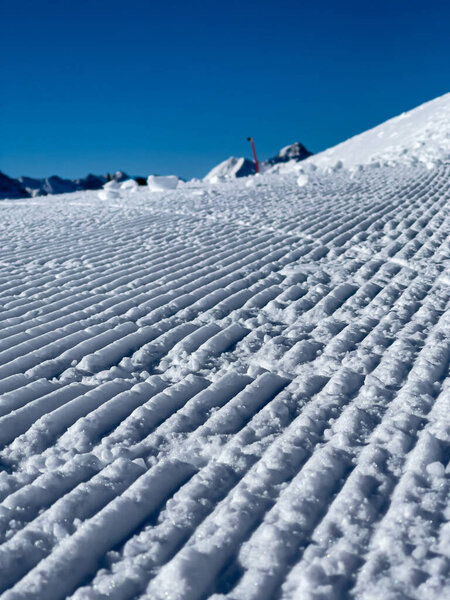 a close up of freshly groomed snow slope and the sky is cloudless and blue