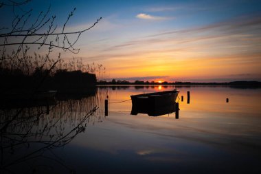a colorful sunset over a lake with rowing boats on the shore