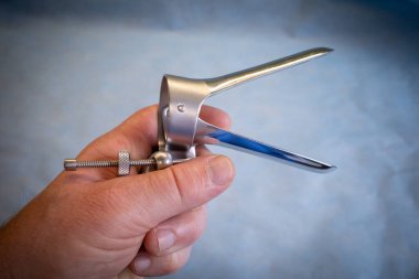 Bir elinde jinekolojik muayene için bir spekulum var.