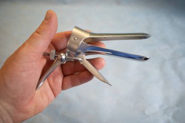 Bir elinde jinekolojik muayene için bir spekulum var.