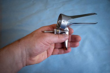 Bir elinde jinekolojik muayene için bir spekulum var.