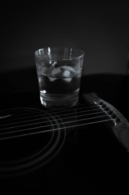 Gitarın üzerinde siyah beyaz buzlu bir bardak viski var.