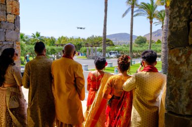 Otelin önünde renkli giyimli Hintli bir düğün grubu gelin ve damadın gelişini bekliyor.