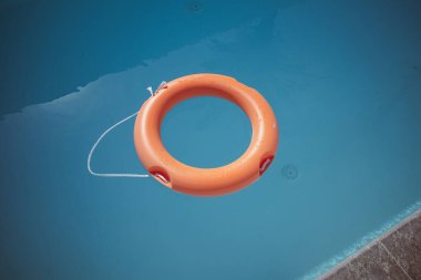 Yüzme havuzunun mavi sularında kırmızı bir yaşam halkası yüzer.