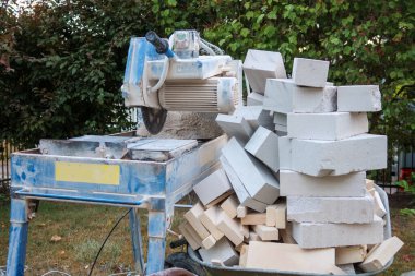 Taşlar için dairesel bir testerenin yanında taş kırıntılarıyla dolu bir el arabası var.