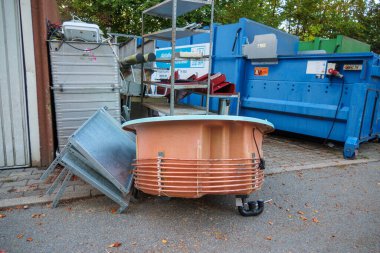 Çöpte, bakır borularla çevrili, atılmış büyük bir küvet var.