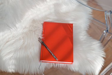 Beyaz arka planda kırmızı kapaklı bir kitap. Kırmızı renkli kağıt günlük ve bir araya getirilmiş siyah renkli tükenmez kalem..