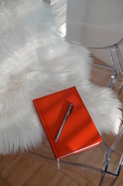 Beyaz arka planda kırmızı kapaklı bir kitap. Kırmızı renkli kağıt günlük ve bir araya getirilmiş siyah renkli tükenmez kalem..