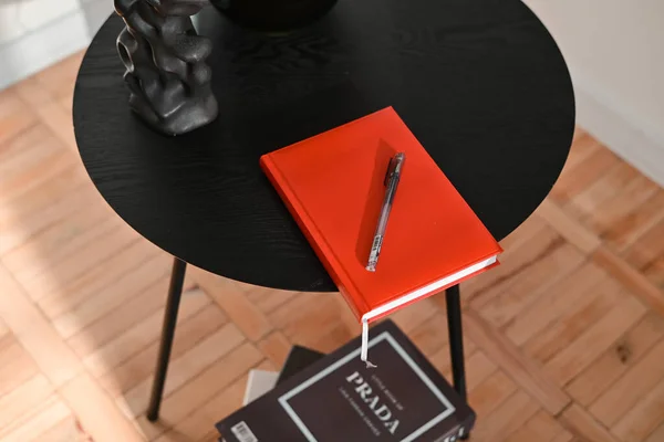 Book in red cover on white background. Red colored note paper diary and a black colored ball point pen placed together.