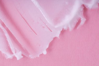 Pembe arka planda krem sürmüş. Kremsi dokusunun makro görüntüsü. 