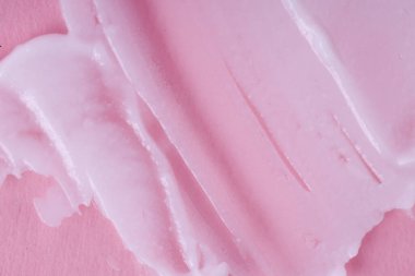 Pembe arka planda krem sürmüş. Kremsi dokusunun makro görüntüsü. 
