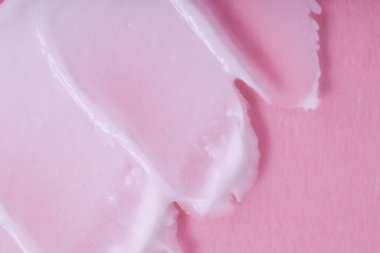 Pembe arka planda krem sürmüş. Kremsi dokusunun makro görüntüsü. 