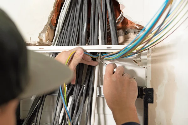 Dangerous work with electricity. The electrician installs the electrical panel and prepares the wires. An electrician is standing near an electrical box