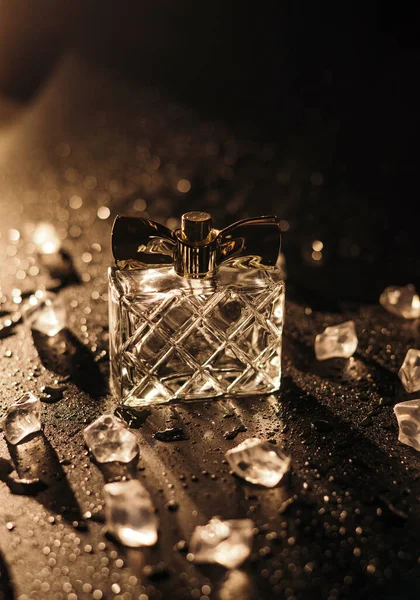 Butelka Kobiecych Perfum Promieniach Złotego Światła Czarnym Tle Kostkami Lodu — Zdjęcie stockowe