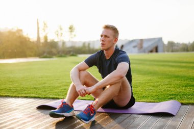 Yorgun adam gün batımında egzersiz ve yoga minderinde dinleniyor..