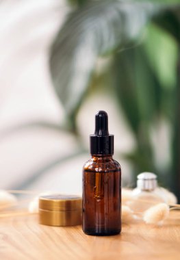 Banyodaki yeşil yaprakların arka planında siyah kauçuk uçlu pipetli kahverengi cam damlacık şişesi. Deri bakımı konsepti. Organik kaplıca ürünleri