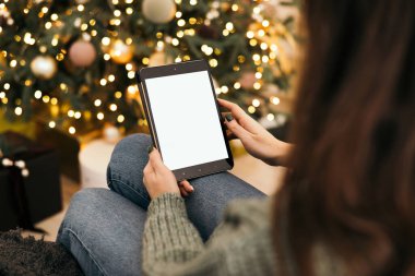 Model, tablet bir kızın elindeydi. Yılbaşı ve Noel ağacının arka planına karşı. Çevrimiçi alışveriş kavramı, indirimler veya İnternet.