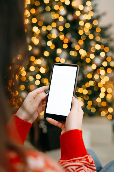 クリスマス モックアップとテキストのためのスペース クリスマス広告アプリのテンプレート 黄金の美しいクリスマスツリーの背景に空の画面で携帯電話を保持する手ライト — ストック写真
