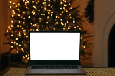 Evde beyaz ekranlı, Noel ağacı ışığında dizüstü bilgisayarın ön görüntüsü. Noel indirimi. İnternetten alışveriş. Yeni yıl ve Noel için hediyeler