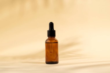 Pipetli kozmetik şişesi. Kahverengi sıvı, cam şişede damlatıcıyla birlikte. Açık bej arka plan ve gölgelerde serum cilt bakımı. Güzellik ürünü maketi