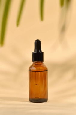 Pipetli kozmetik şişesi. Kahverengi sıvı, cam şişede damlatıcıyla birlikte. Açık bej arka planda serum cilt bakımı ve gölgeler. Güzellik ürünü maketi