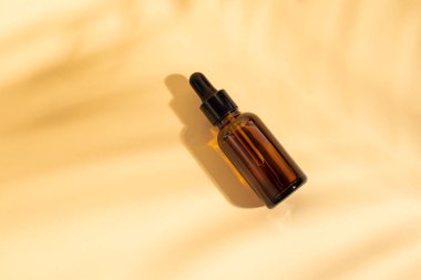 Pipetli kozmetik şişesi. Kahverengi sıvı, cam şişede damlatıcıyla birlikte. Açık bej arka plan ve gölgelerde serum cilt bakımı. Güzellik ürünü maketi