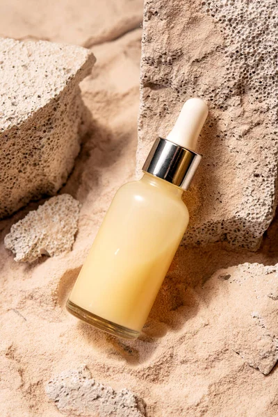 Dropper bottle of moisturizer, serum for face on stones with sand, sand background, summer face care.