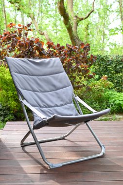 Folding chair surrounded by green leaves on a wooden deck. Relaxation in the garden. Cottage aesthetics. Vacation outside the city. Warm summer day. terrace
