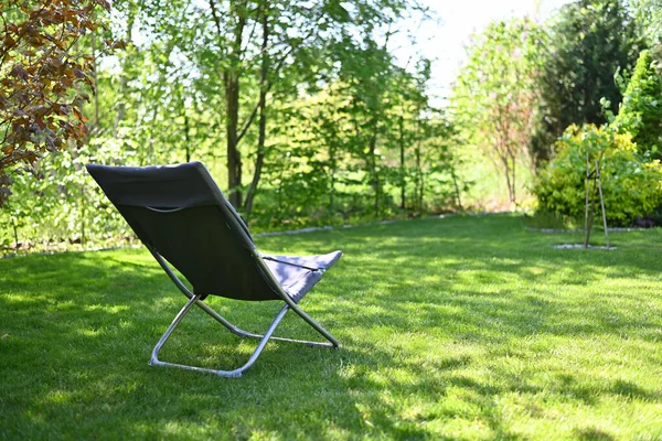 Folding chair surrounded by green leaves in a garden. Relaxation in the garden. Cottage aesthetics. Vacation outside the city. Warm summer day.