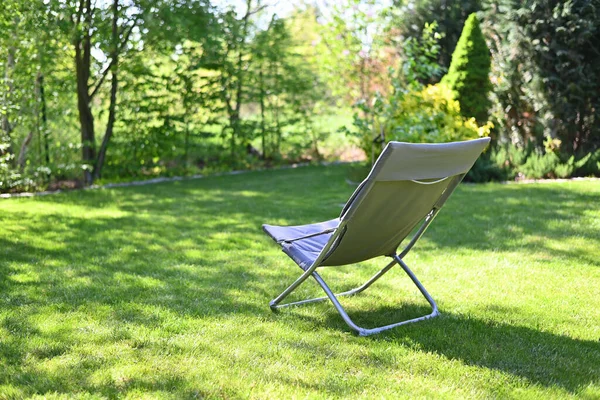 Folding chair surrounded by green leaves in a garden. Relaxation in the garden. Cottage aesthetics. Vacation outside the city. Warm summer day.