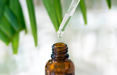 Kozmetik pipeti, yeşil bitkilerin ve banyonun arka planına karşı beyaz bir masada duran kahverengi bir serumun üzerinde..