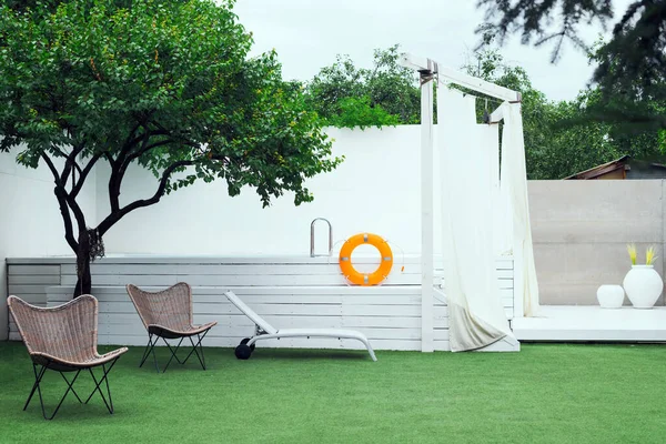 Fenced yard with a beautiful white pool and a green lawn with chairs and sunbeds. High quality photo