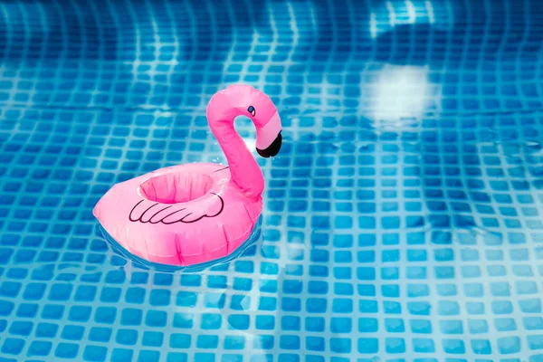 Pink inflatable flamingo in pool water for summer beach background. Minimal summer concept .