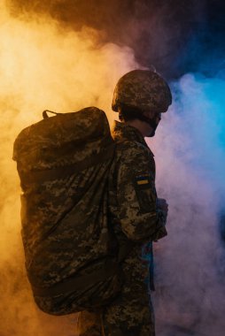Armed Forces of Ukraine. A close-up photo of a military man in the shape of a pixel with military  backpack in colored smoke. Defender of Ukraine