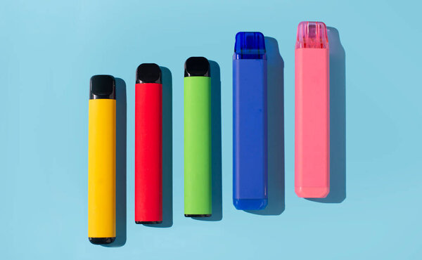 Set of colorful disposable electronic cigarettes on a blue background. The concept of modern smoking. Top view.