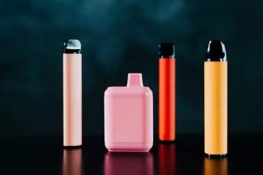 A set of colorful disposable electronic cigarettes of different shapes on a black background with smoke. 