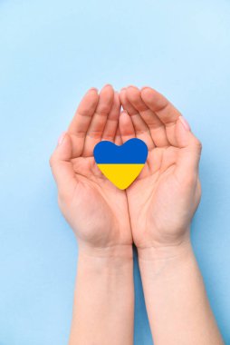 The female hand holds a heart of a yellow-blue Ukrainian flag on blue background. The concept of participation of the Ukrainian people in the war with russia. stop war