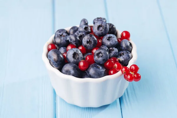 Assorted berries in white bowl on wood: blueberry and red currant on blue wood background. Summer Freshly Berry. High quality photo