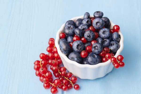 Assorted berries in white bowl on wood: blueberry and red currant on blue wood background. Summer Freshly Berry. High quality photo