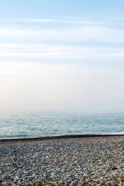 Seascape view of nature on the coast of a beach and ocean water on a Summer day. Beautiful scenery of a sea shore filled with rocky sand textures and the blue sky on the horizon and fog