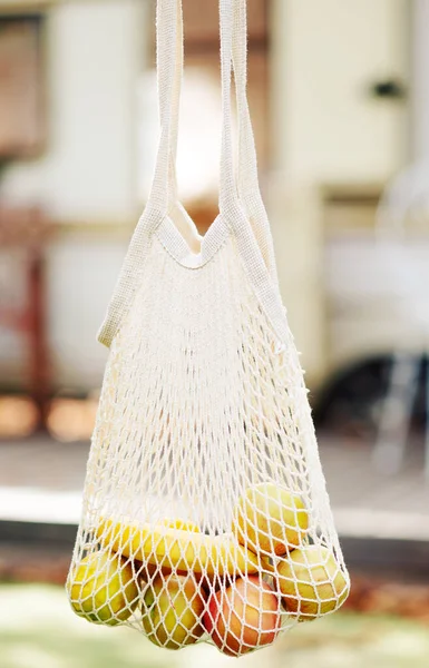 Mesh bag with fruits in female hand. hold mesh shopping bag on light background. Modern reusable shopping, zero waste concept